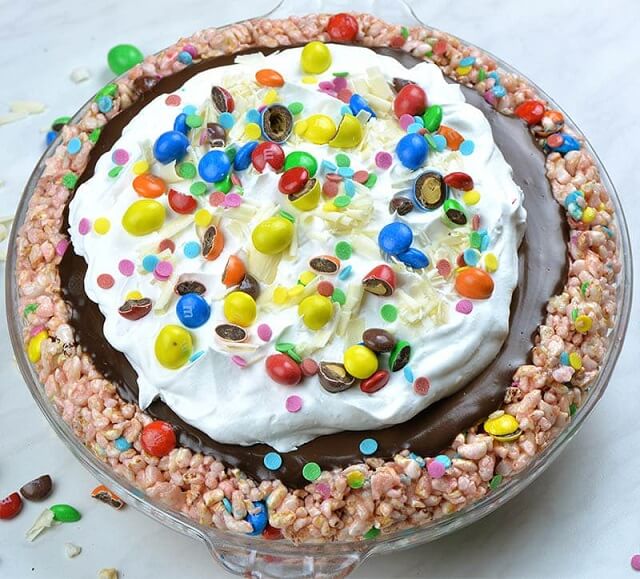 Rice Krispie crust, chocolate filling, whipped cream, confetti sprinkles, M&M candies, and white chocolate shavings
