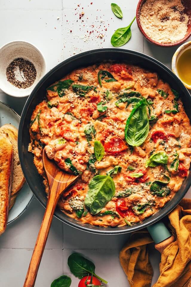 Deliciously creamy vegan skillet dish featuring white beans burst cherry tomatoes, and vibrant greens, all embraced by a flavorful cashew sauce.