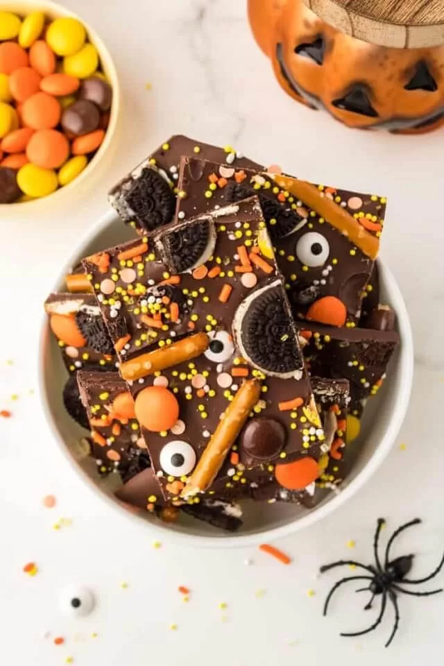 Melt the chocolate and spread it on a baking sheet. Then, top with Halloween candy, sprinkles, and pretzels.