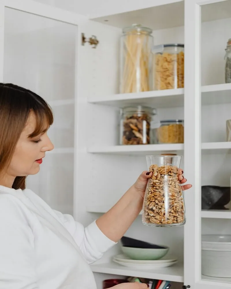 A woman looking at a clear glass of nuts for a minimalist pantry assembly.